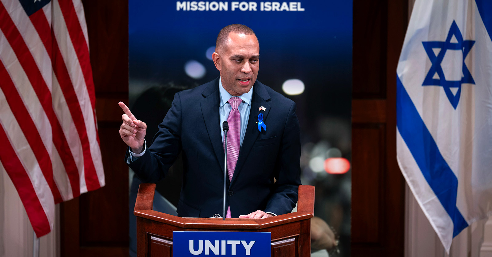 Picture of Hakeem Jeffries speaking at conference between U.S. and Israeli flags